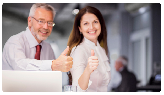 Two colleagues smiling and giving a thumbs up beside a laptop